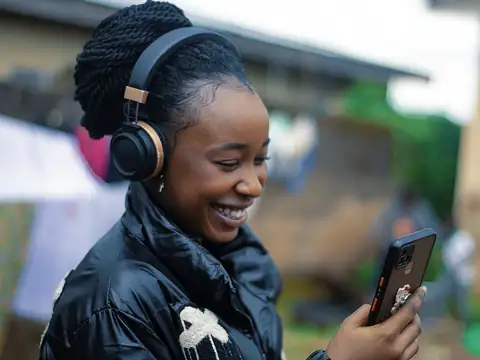 Une élève souriante, avec un casque audio, regarde son téléphone