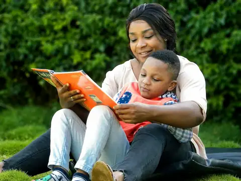 Une maman lit un livre avec son fils, installés ensemble sur l'herbe